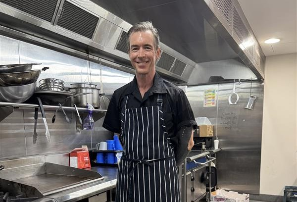 Man in chef uniform standing in kitchen with smile on his face