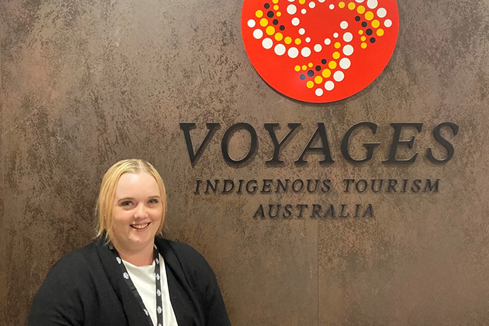Photo of customer Jasmine standing in front of a Voyages Indigenous Tourism Australia sign