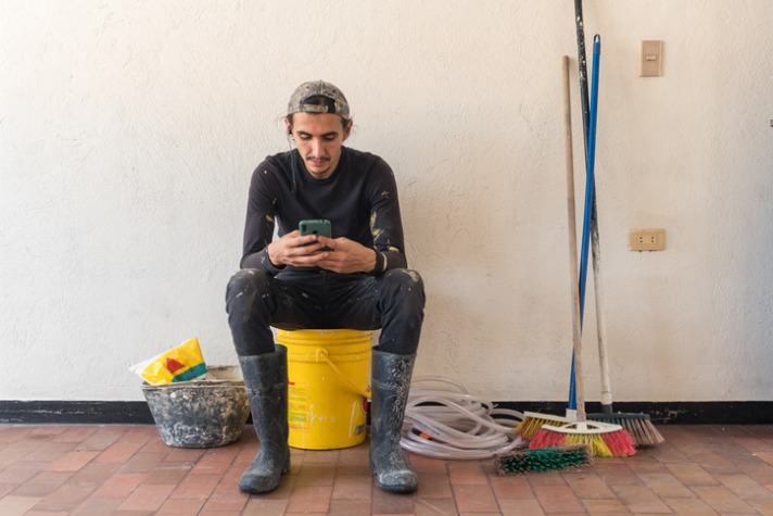 worker sitting on a bucket playing with phone