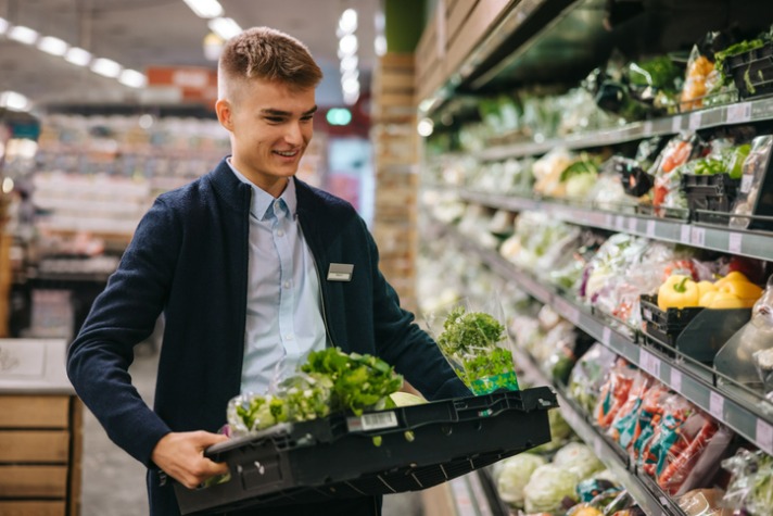 what are the 8 different types of employment image of Shop assistant in supermarket re-stocking fresh vegetables in shelves of produce section.