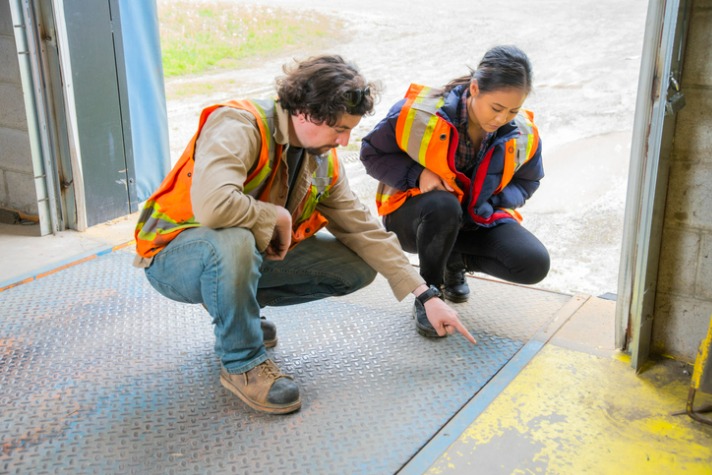An industrial warehouse workplace safety topic. A supervisor or manager explains the danger involved with lifting and dropping loading dock plates safety in the workplace
