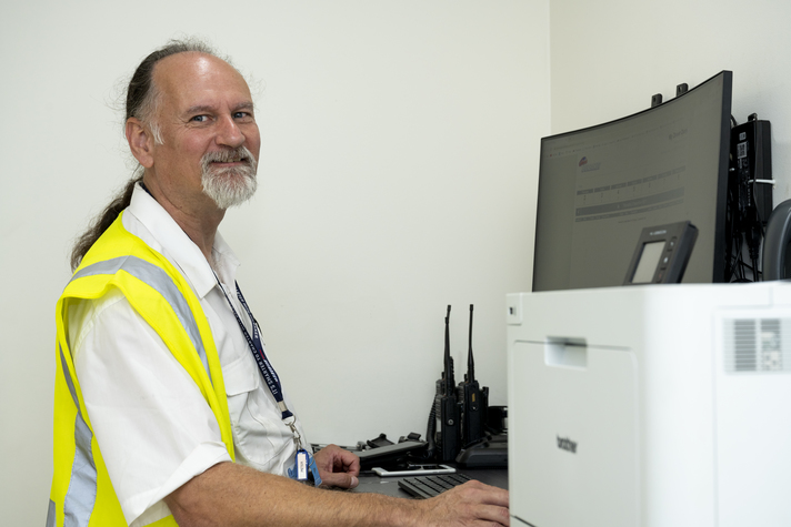 customer Peter Belbaker in hi vis vest smiling working on computer